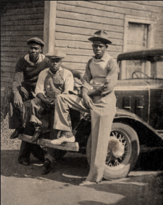 three men sitting on front bumper of car